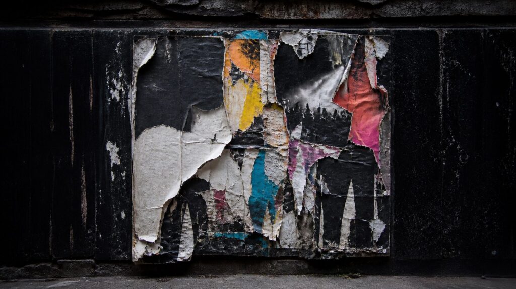 A wall of layered concert posters weathered by rain, older sheets torn open to reveal decades of pasted paper underneath